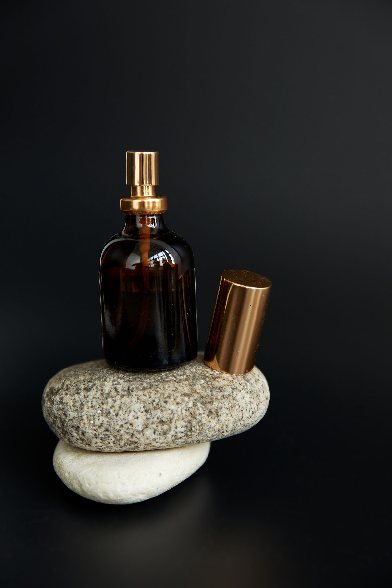 Frasco ámbar con tapón dorado sobre piedras, fondo oscuro