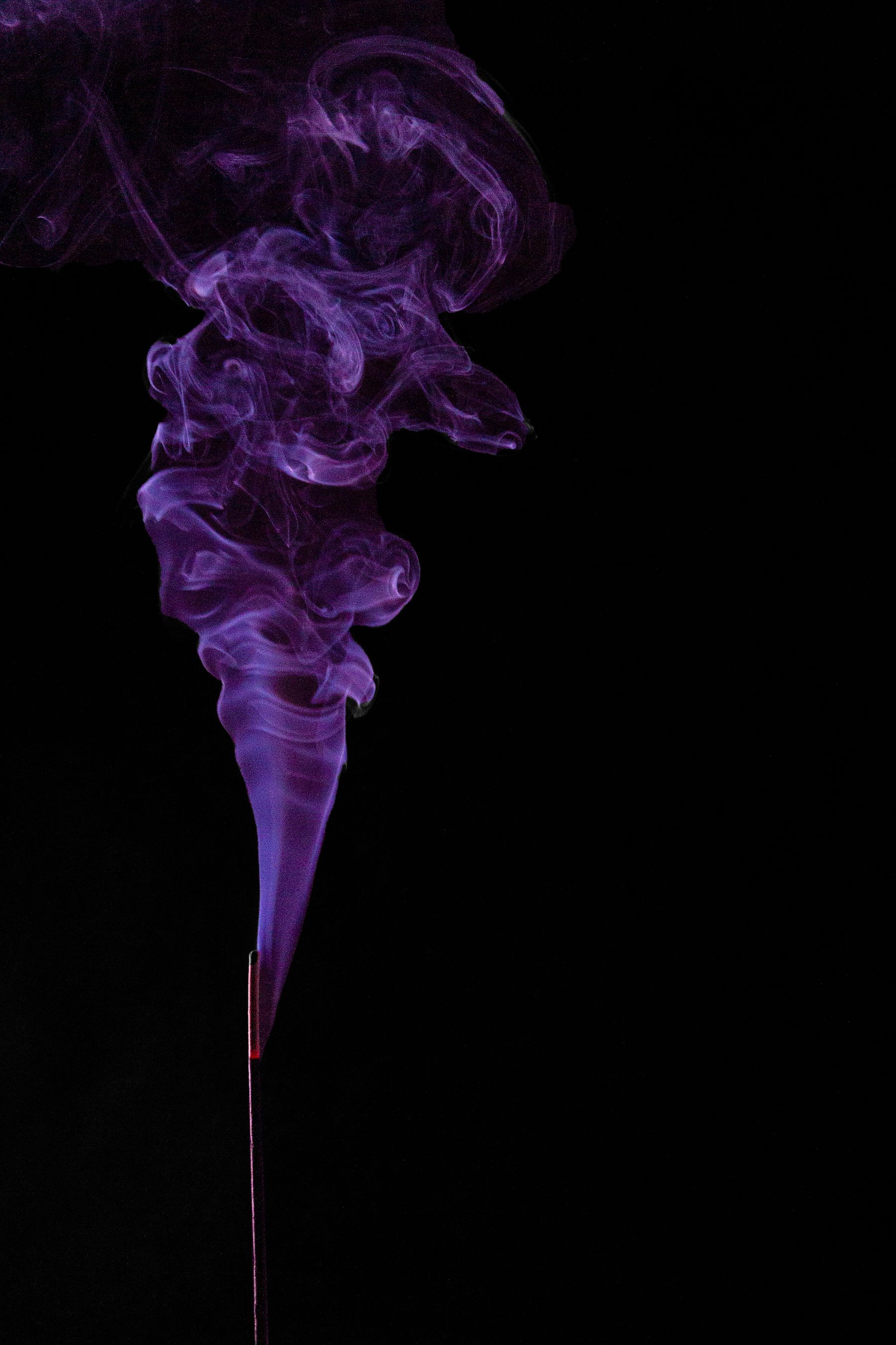 Hilo de humo violeta ascendiendo desde una varilla de incienso encendida